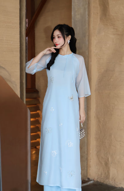 Woman wearing a light blue dress with floral patterns in an indoor setting.