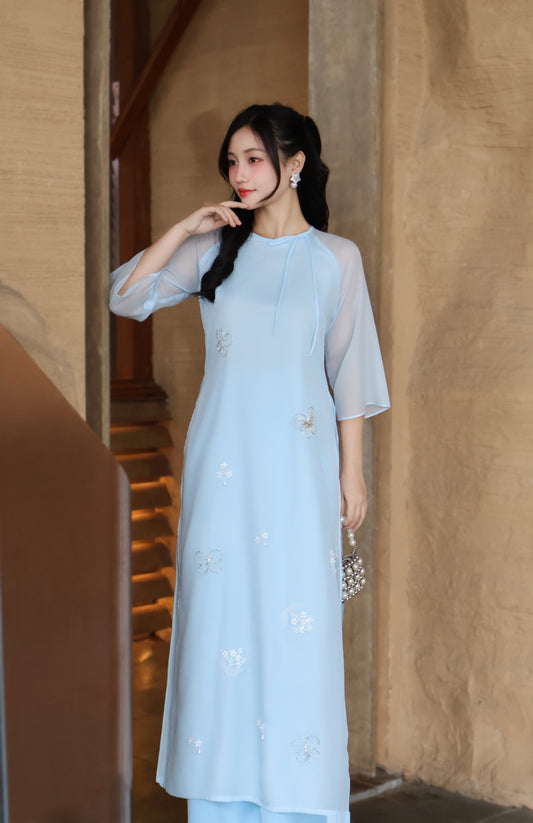 Woman wearing a light blue dress with floral patterns in an indoor setting.